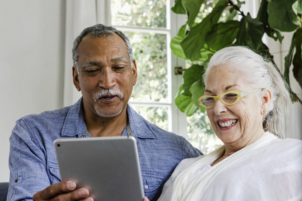 Elderly couple using a tablet on a couch, looking up information about Medicare open enrollment periods.