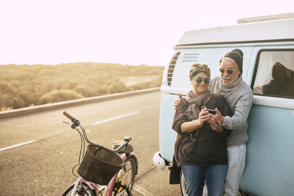 Older couple standing by their VW CamperVan looking at their phone to see if they qualify for Medicare and Medicaid.