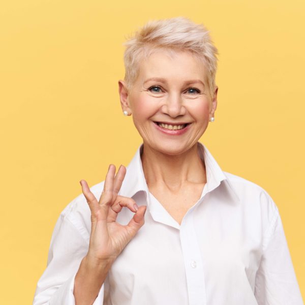 Portrait of successful confident middle aged businesswoman with short dyed hair looking at camera with broad smile making ok gesture, rejoicing at good profitable deal and great yearly income