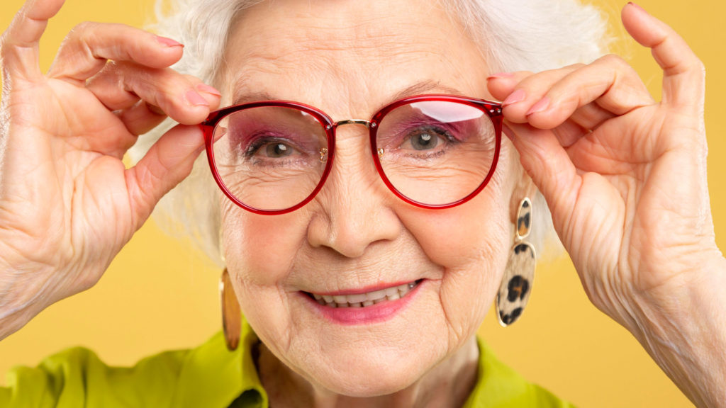Older woman holding up glasses to her face.