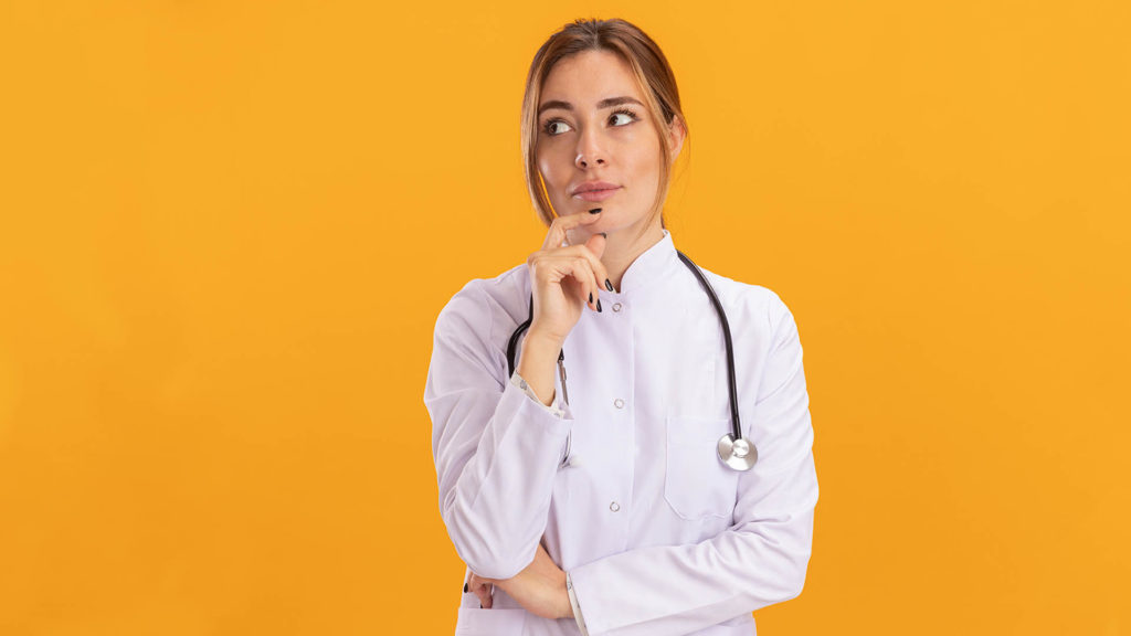 impressed looking at side young female doctor wearing medical robe with stethoscope grabbed chin isolated on yellow background
