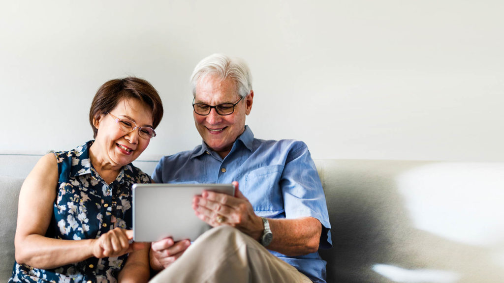 Senior couple using a digital device in a living room reading up on "What are Medical Groups."