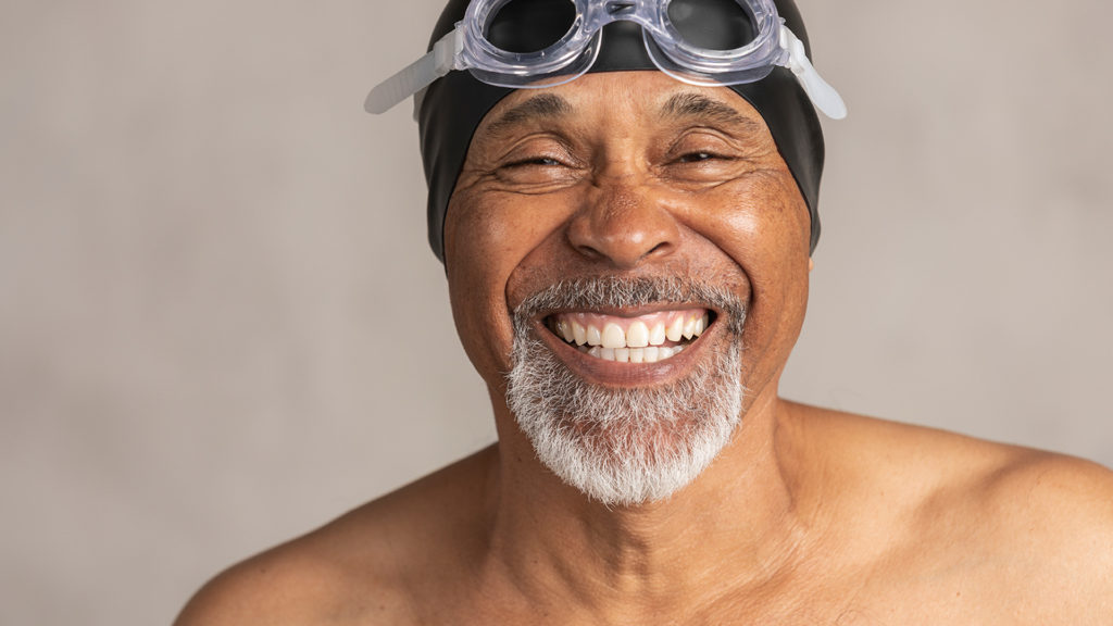 Senior African American swimmer wearing a swim cap and goggles, laughing.