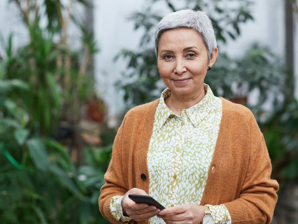 Older woman holding cell phone and looking at camera.