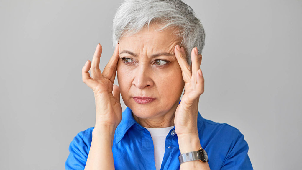 Photo of older woman with her fingers on her temples wondering why Medicare Plan F is going away.