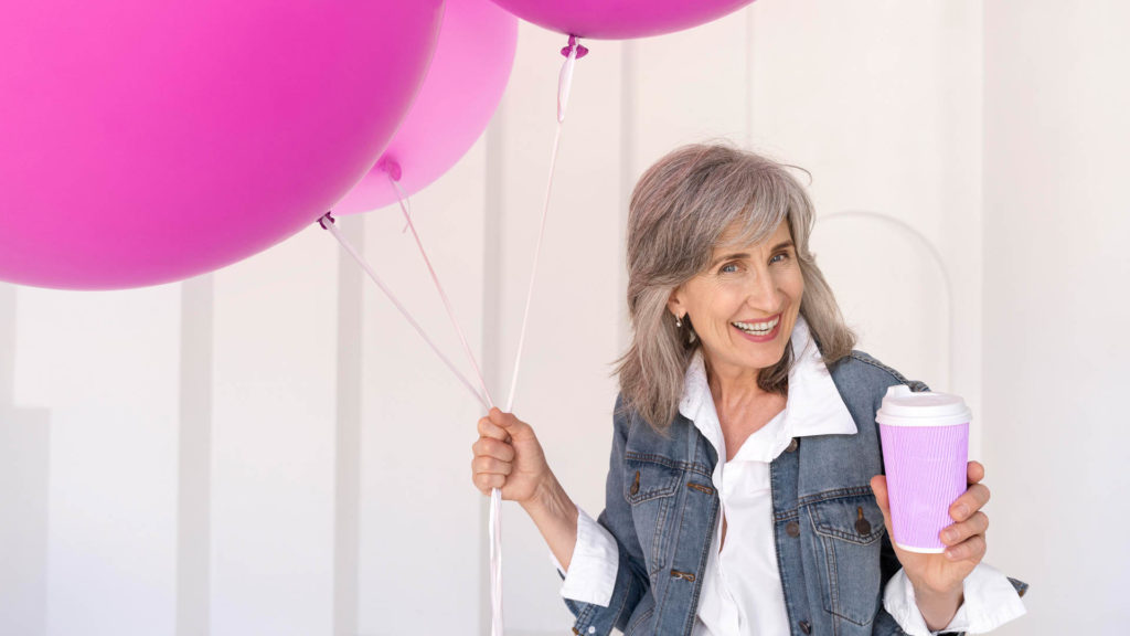 Senior woman with pink balloons and pink coffee cup, smiling about her ability to Choose Between Medicare Advantage & Medicare Supplement Plans