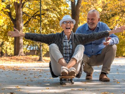Senior couple outside with woman sitting on a skateboard.