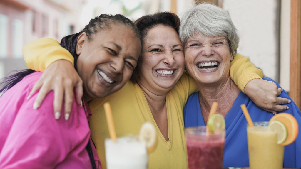 Three senior females smiling over lunch and a chat about Medicare Fall Open Enrollment.
