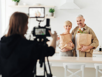 Director filming seniors holding grocery bags in their kitchen as they discuss the truth about Medicare commercials.