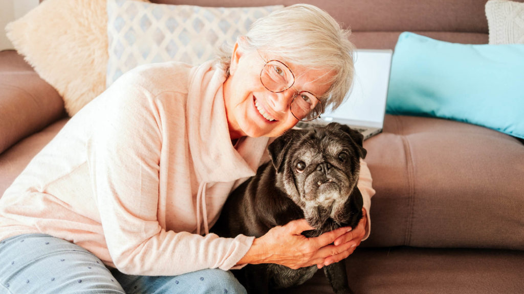 Older woman smiling and hugging her dog after she received her social security check with her Medicare Advantage give back plan money.