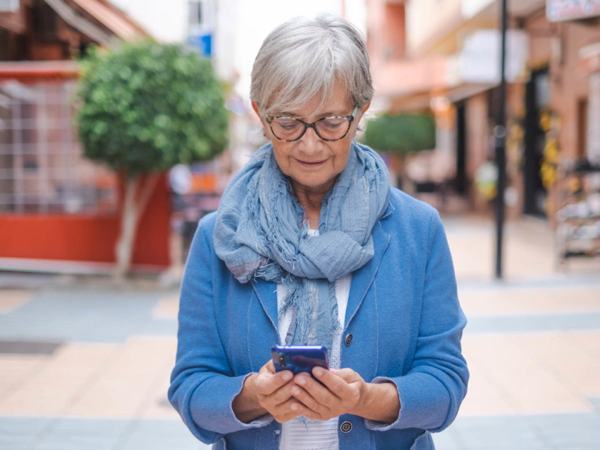 Older woman in glasses searching her phone for "Does Medicare Cover Vision?"